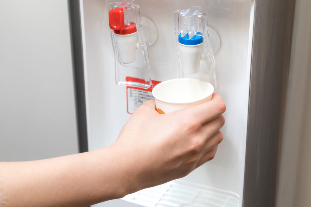 ウォーターサーバーから紙コップに水を注いでいる手元